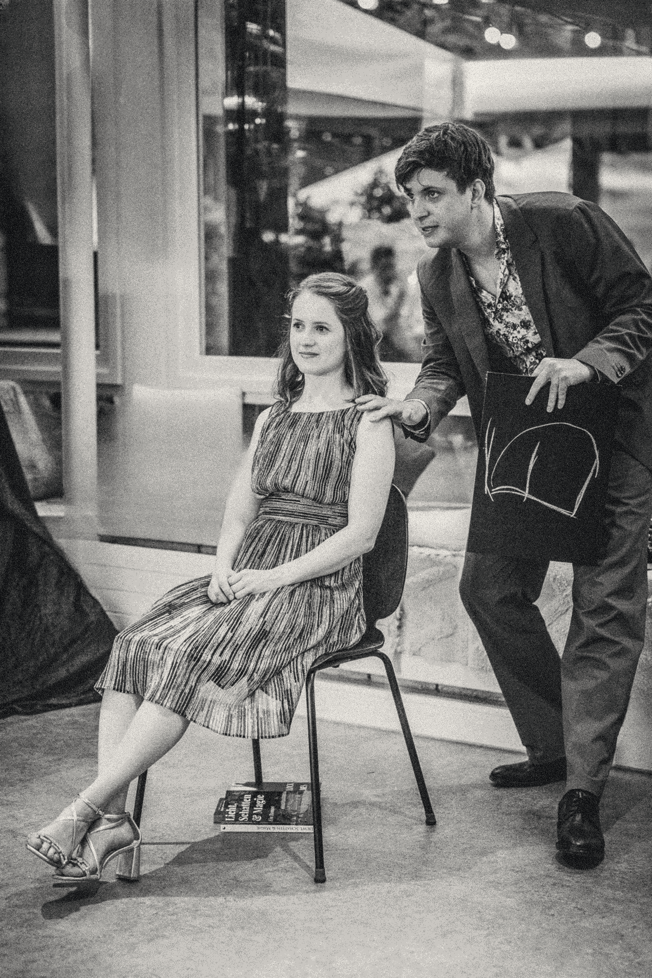 Junge Frau sitzt auf einem Stuhl - TOM steht daneben mit einer Kreidetafel in der Hand.