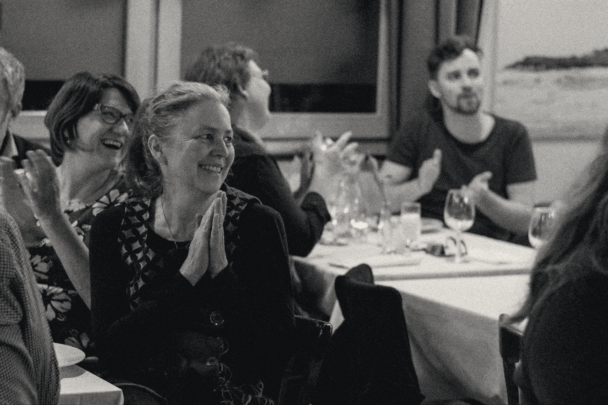 Zwei Frauen sitzen an einem Tisch, lachen und klatschen.