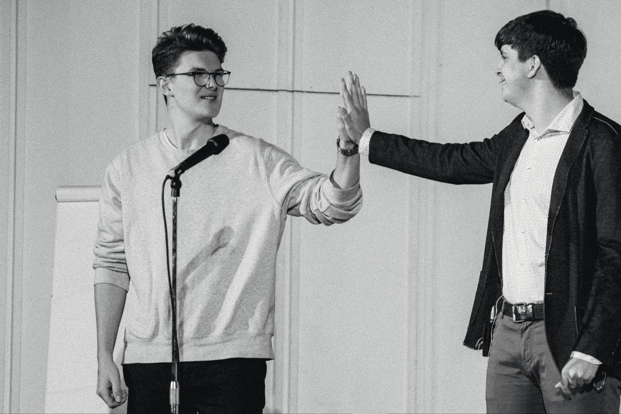 TOM und ein junger Mann stehen nebeneinander auf der Bühne - Handflächen aneinander gedrückt.